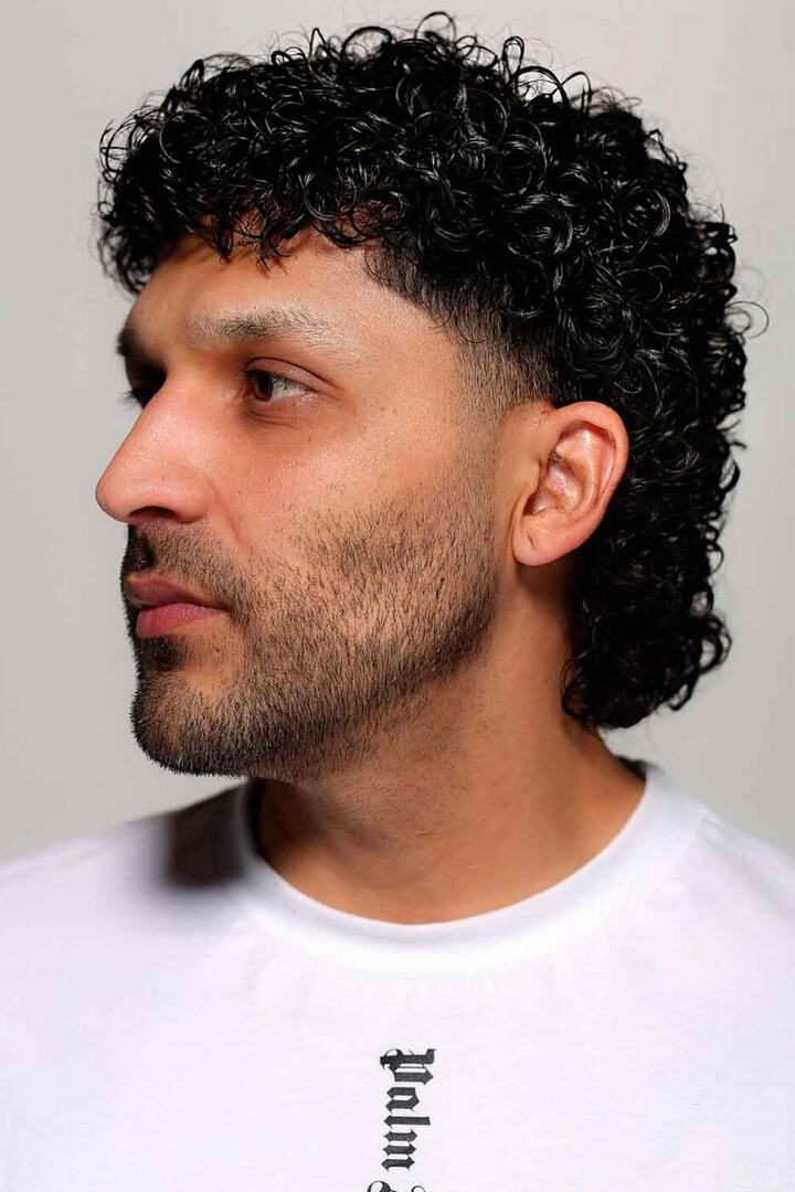 Uomo con mullet ricci e t-shirt bianca come base di stile